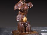 bronze sculpture of a female torso holding an apple on a wooden base