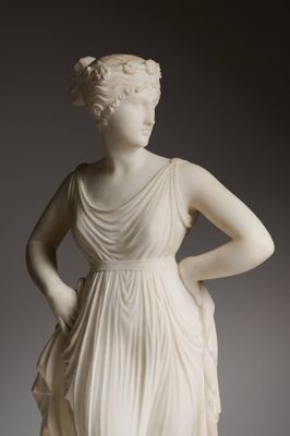 une statue représentant une femme en robe blanche, les mains sur les hanches