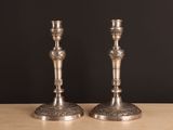 une paire de bougeoirs en argent posés sur une table, sur fond noir