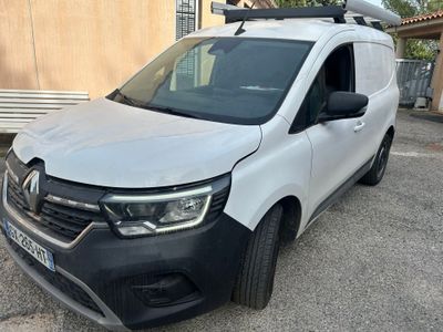 La camionnette blanche est garée devant un immeuble ; elle est équipée d'une galerie de toit.