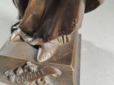 bronze statue of a woman holding a flower in her right hand