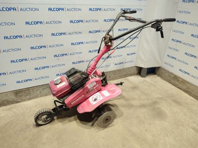 the small pink mower is parked in front of a wall