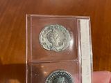 someone is holding two silver coins in a clear box on a table