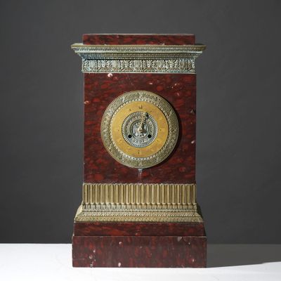 une horloge rouge et dorée posée sur une table blanche