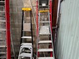 Plusieurs échelles sont alignées contre un mur, à côté d'un immeuble.