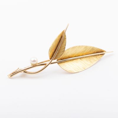 a close up of a gold leaf brooch with a pearl