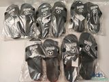 six paires de chaussons noirs et blancs dans des sacs en plastique, posées sur une surface blanche