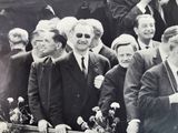 black and white photograph of a group of men in suits and ties standing in front of a crowd of people
