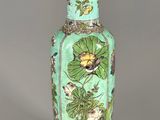 a green vase with flowers and leaves on it