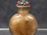 un petit vase en verre avec un couvercle en argent, posé sur une table