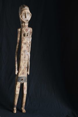 une statue en bois représentant un homme debout devant un fond noir