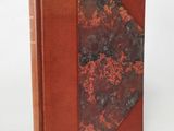 an old book with a red cover sitting on top of a white surface