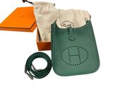 a green purse with a belt and a bag in front of it