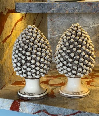 two white vases that have pine cones on them