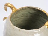 a white vase with a gold handle on a white surface