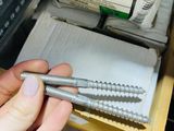 a person holding a screw in their hand in front of a box of screws