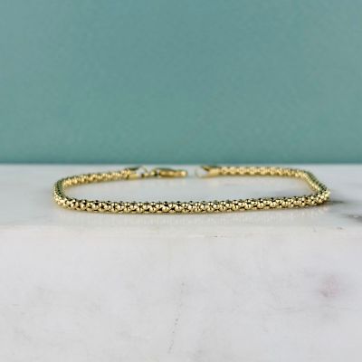 un gros plan d'un bracelet en or posé sur une surface en marbre