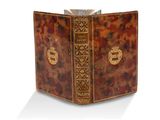 un vieux livre à la couverture décorative posé sur une surface blanche