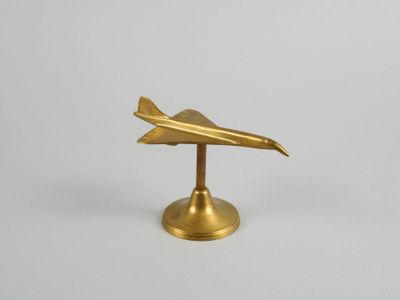 figurine d'avion en laiton posée sur un socle, sur fond blanc