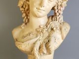 un buste en marbre blanc représentant une femme aux cheveux bouclés, posé sur un socle
