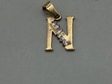 a close up of a gold pendant with a letter n on it