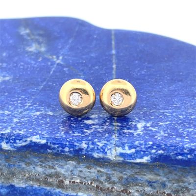 pair of gold and diamond stud earrings sitting on top of a blue stone