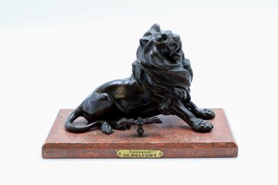 statue en bronze représentant un lion, posée sur un socle en marbre, sur fond blanc