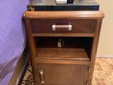 a nightstand with a phone on top of it next to a bed