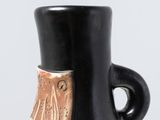 a black vase sitting on a white table with a brown handle
