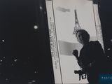 black and white photograph of a woman standing in front of a picture of the eiffel tower