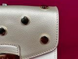 a white and red purse with studded handles on a pink background