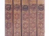 six old books are lined up in a row on a white surface