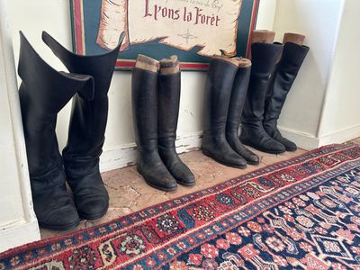 Plusieurs paires de bottes sont alignées contre un mur, près d'un tapis