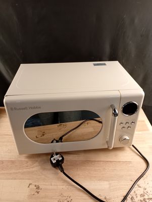un micro-ondes blanc posé sur une table en bois, avec un cordon noir