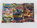 trois paquets de cartes à collectionner Pokémon posés sur une surface blanche