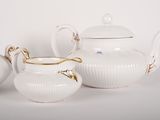 three white porcelain teapots with gold trim and lids on a white surface