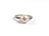 une bague en perle blanche et diamants posée sur une surface blanche