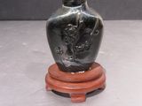 a small black vase on a wooden stand on a table