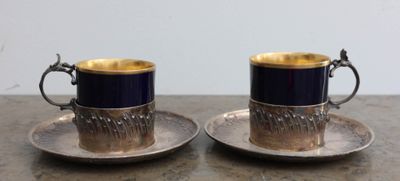 une paire de tasses et soucoupes plaquées argent posées sur une table