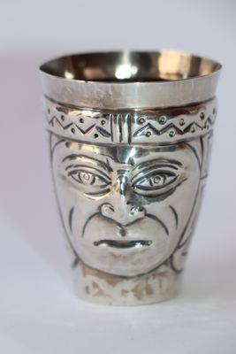 une coupe en argent ornée d'un visage, posée sur une table