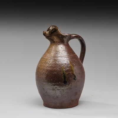 un vase marron muni d'une anse marron, posé sur une surface blanche