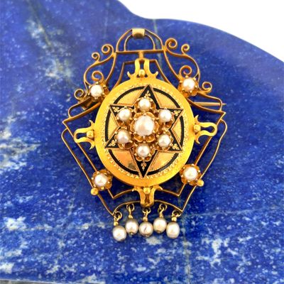 a close up of a gold and pearl broochle on a blue stone