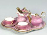 a pink tea set on a tray on a white table