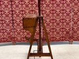 an old wooden easer with a wooden seat and a red wallpaper behind it