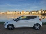 the white car is parked near the water in front of the city