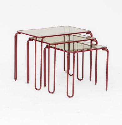 un ensemble de trois tables gigognes en métal rouge avec des plateaux en verre