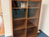 a wooden bookcase with a glass door in the corner of a room