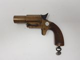 un vieux revolver en laiton avec une crosse en bois, posé sur une surface blanche
