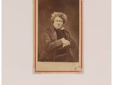 une vieille photo d'une femme aux cheveux bouclés, assise devant une table