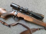 a close up of a rifle with a scope and a sling on the ground